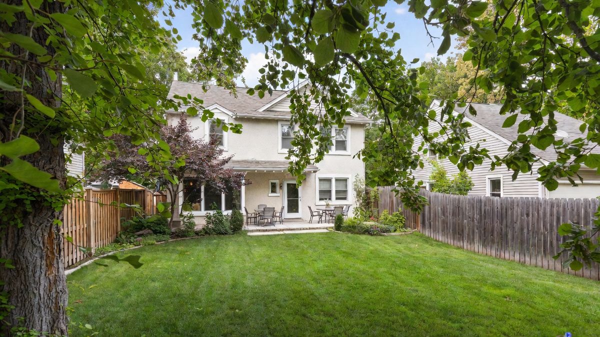 Private fenced backyard in Grimes Iowa with mature trees, patio seating, and lush green lawn